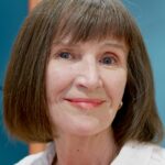 Menu Portrait of a smiling senior woman with short brown hair indoors captured in a friendly close-up.